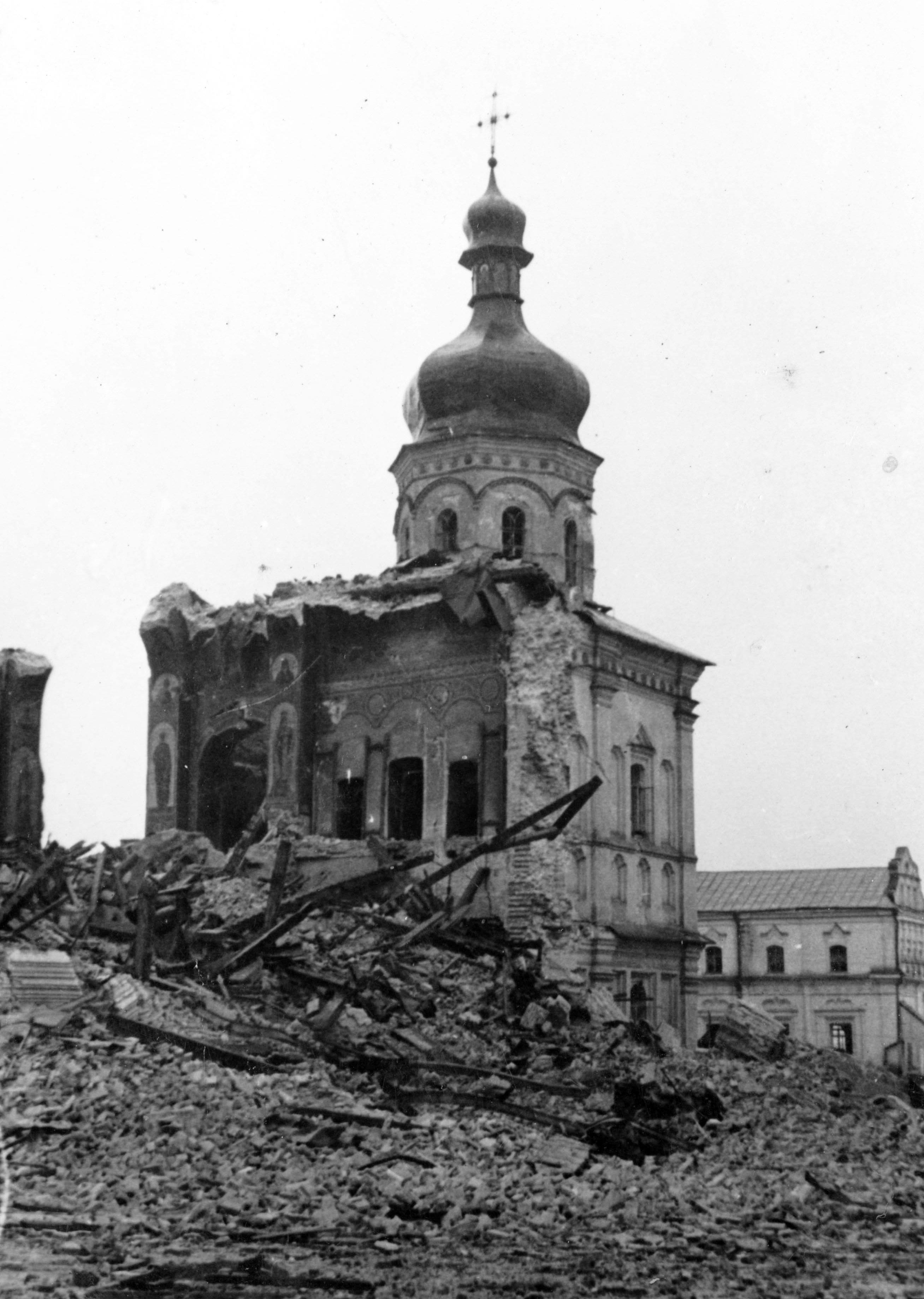 Black-and-white photograph of the Dormition Cathedral ruins: a surviving onion-domed tower above frescoed walls and a field of rubble, 1942.