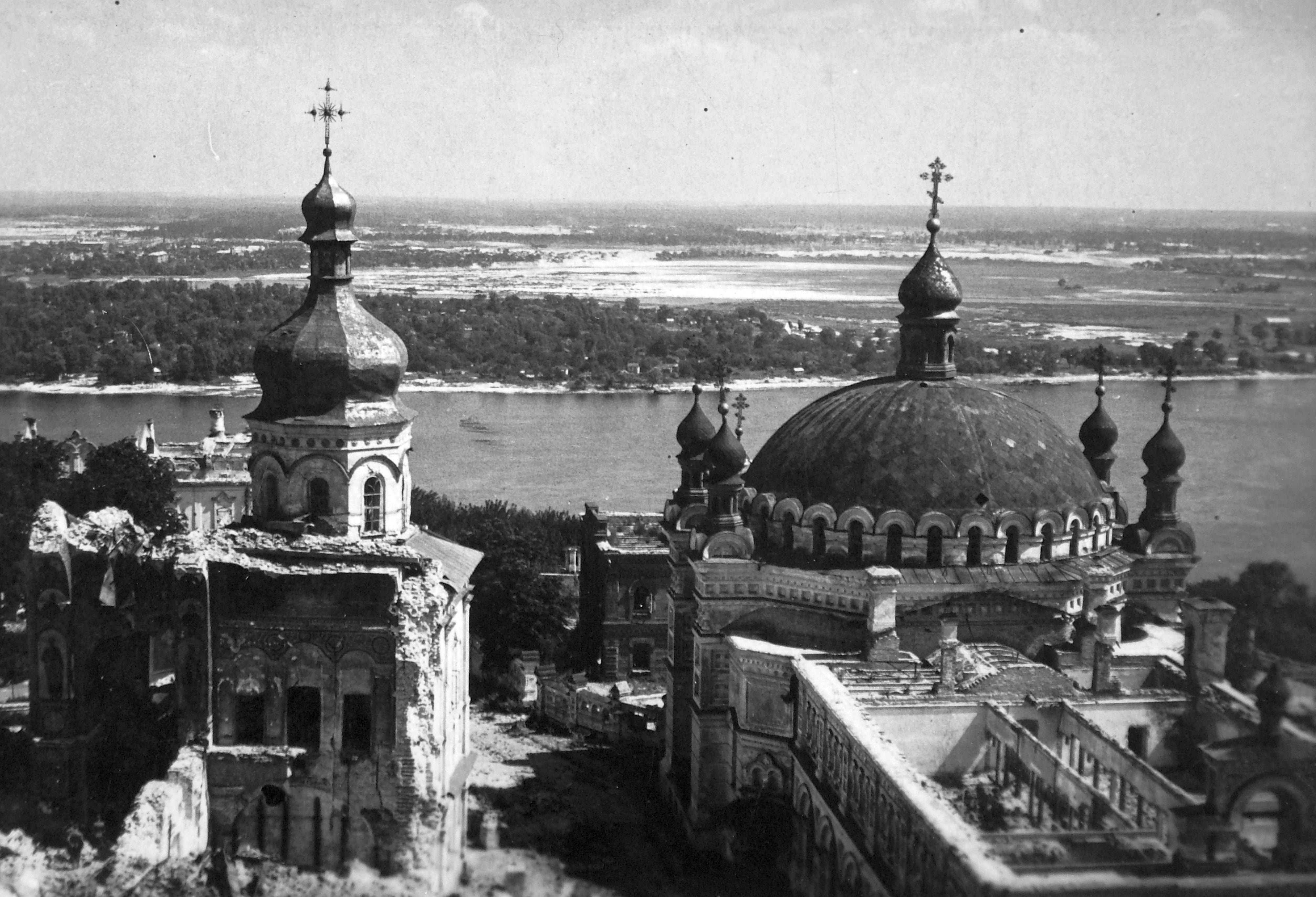 Elevated black-and-white view of the Lavra grounds — the destroyed cathedral at left, the domed Refectory Church at right, the Dnipro behind.