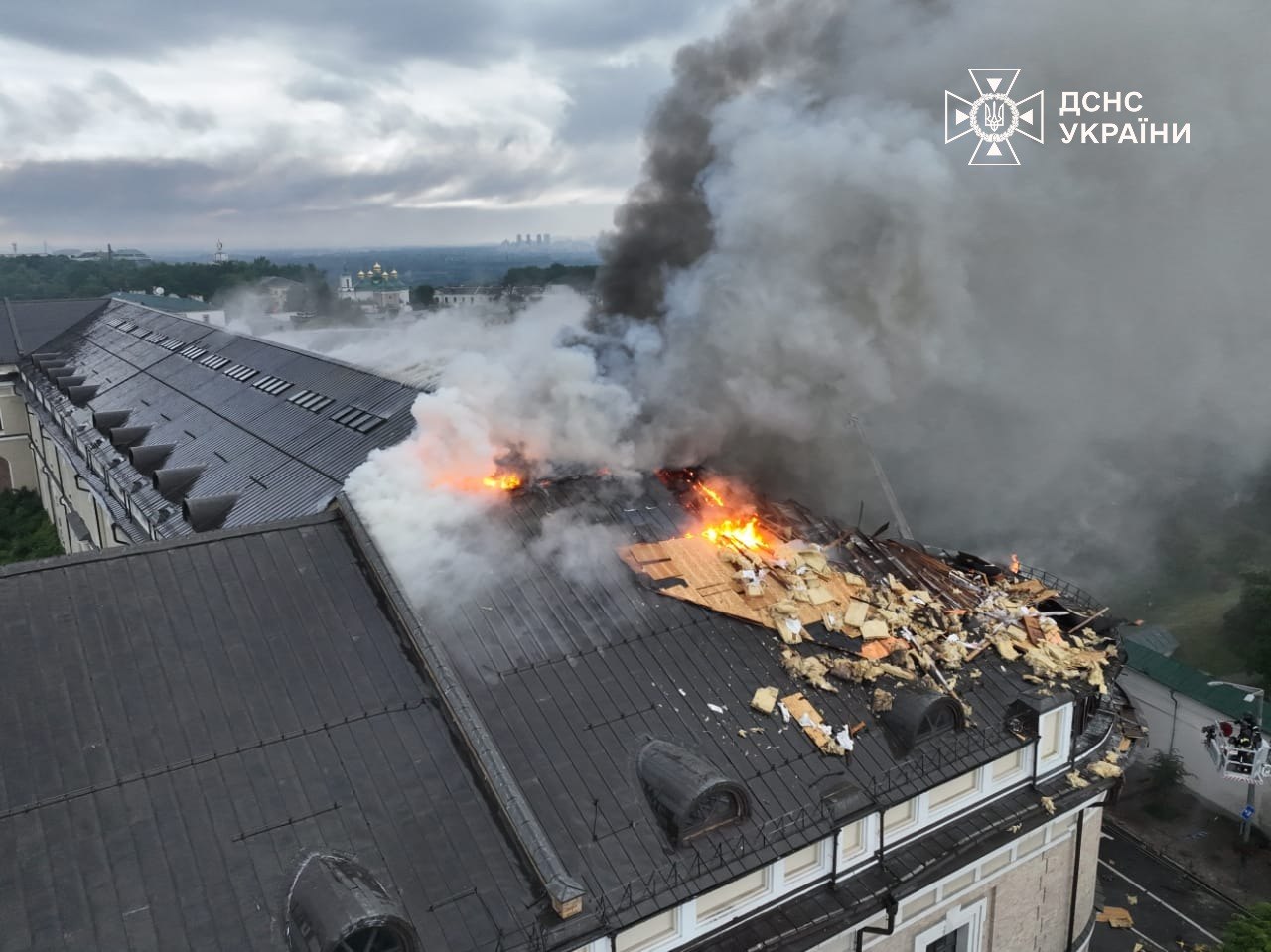 Aerial drone view of the torn-open, burning roof of the Mystetskyi Arsenal beside the Kyiv-Pechersk Lavra, flames, smoke and scattered debris, the Lavra domes beyond, 15 June 2026.